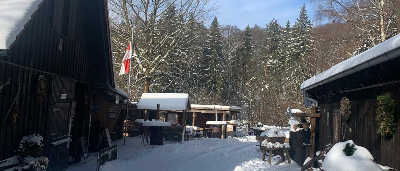 Schneebedeckter Weg zwischen Holzhütten, umgeben von verschneiten Bäumen im Wald.