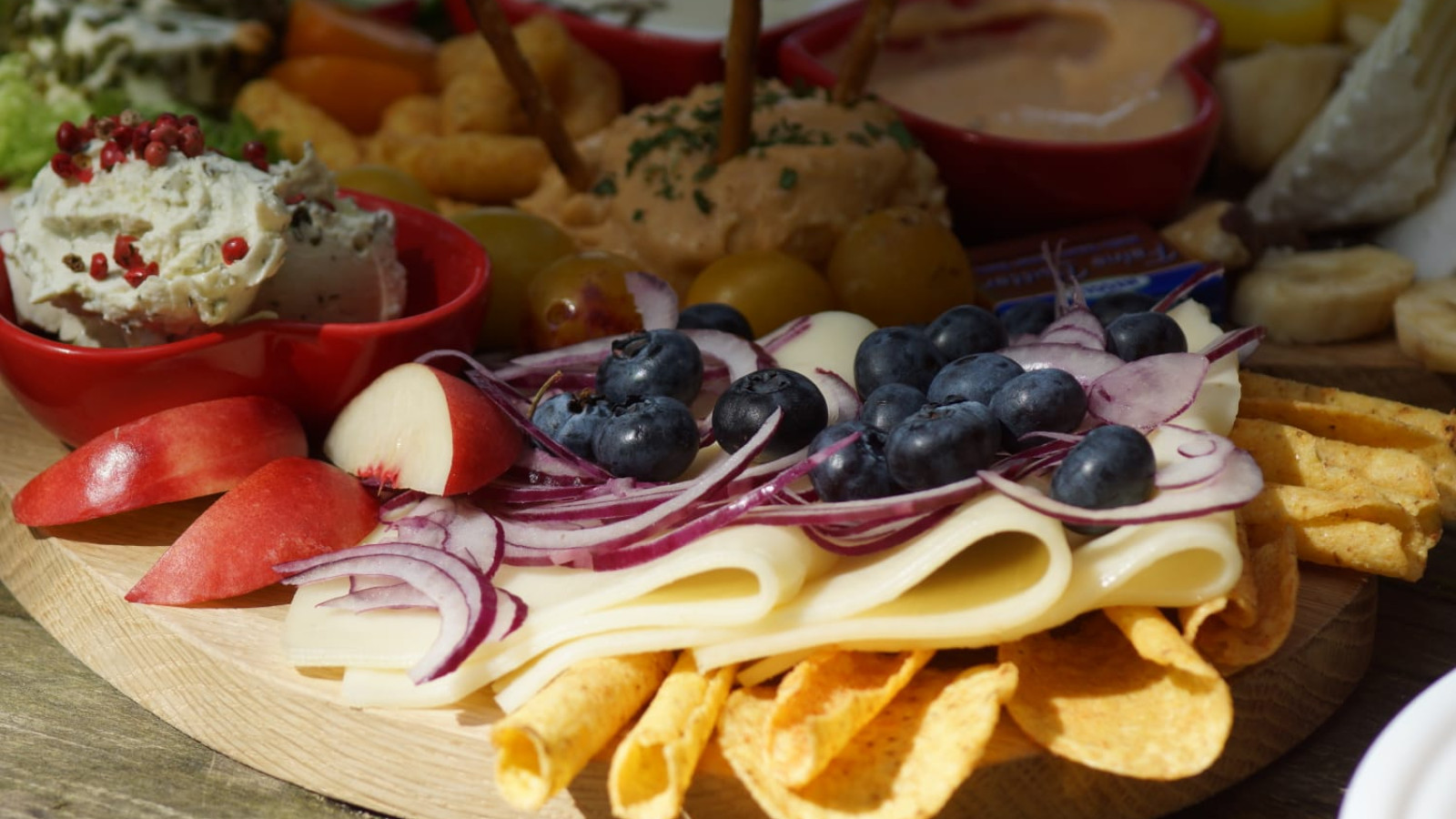 Buffet mit Käse, Blaubeeren, roter Zwiebel, Frischkäse und Crackern auf einem Holztisch.