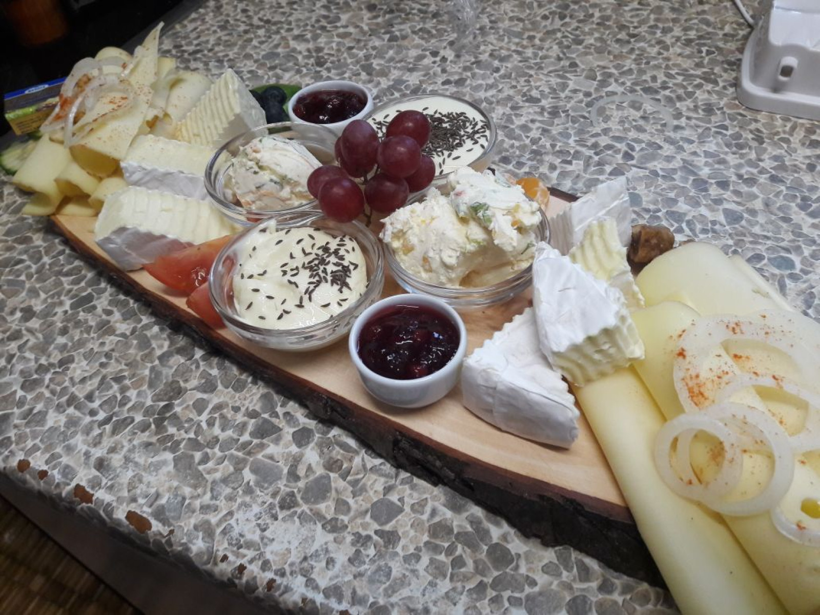 Eine dekorative Käseplatte mit Trauben, verschiedenen Käsesorten, Aufstrichen und Marmelade.