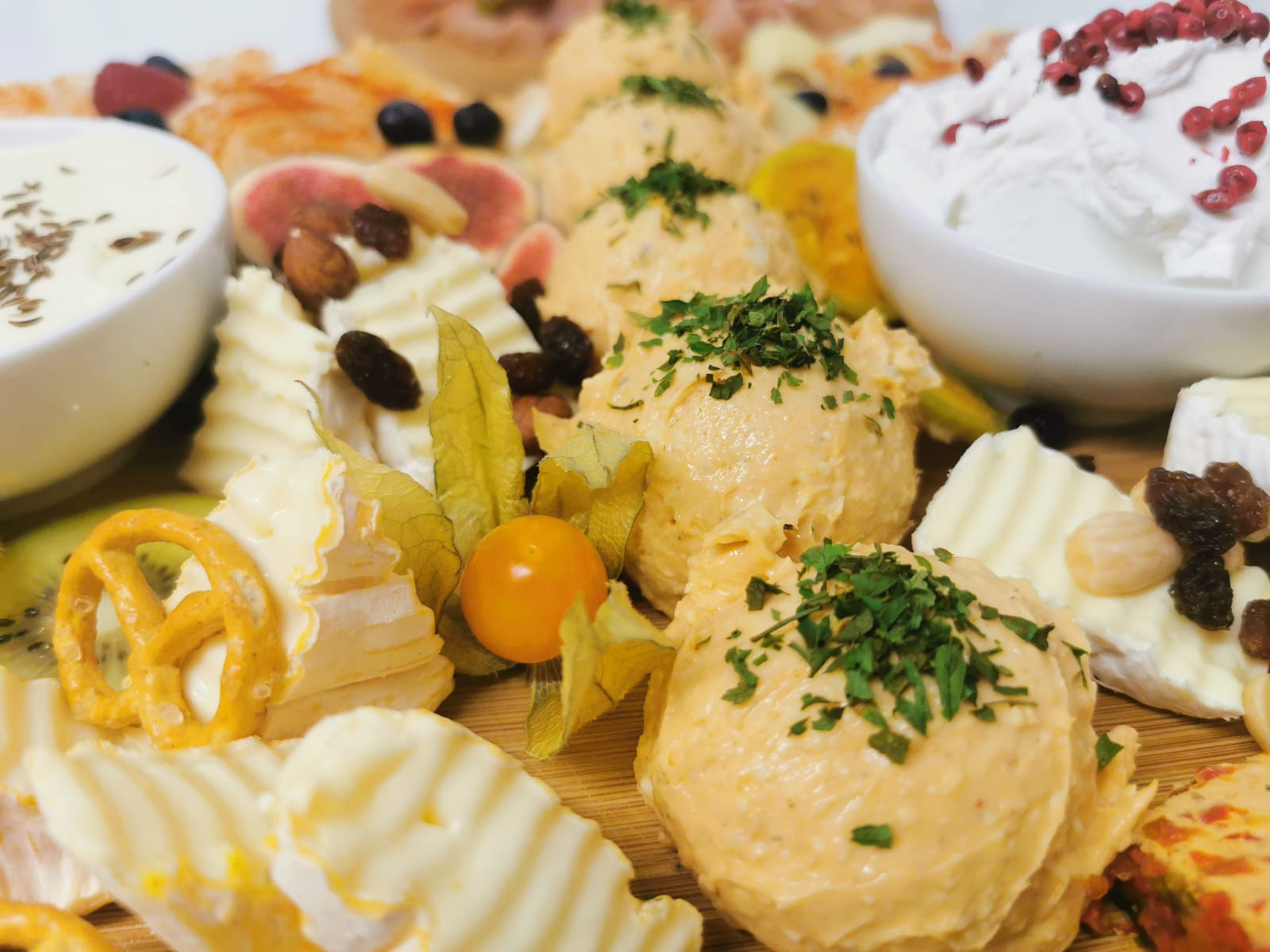 Naheaufnahme einer Käseplatte mit verschiedenen Käsesorten, Früchten und Nüssen auf Holzbrett.