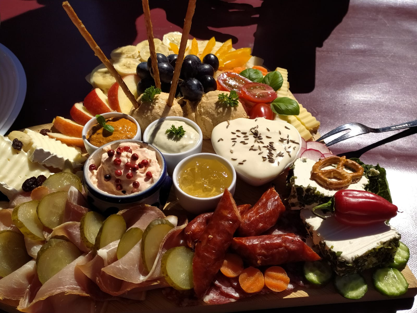 Käse- und Wurstplatte mit Dips, Obst, Gemüse und Brotsnacks auf einem Tisch.
