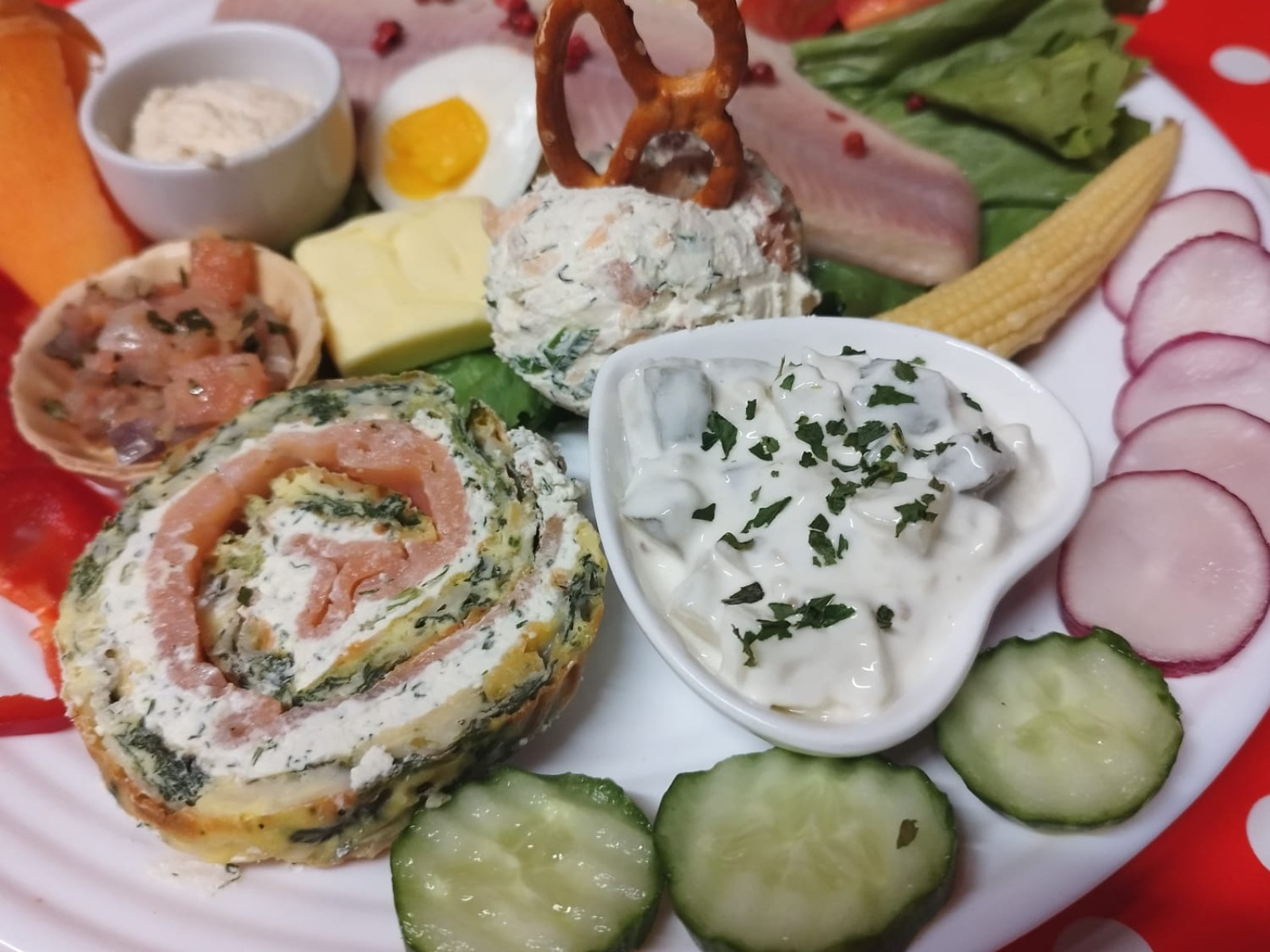 Ein Teller mit verschiedenen kalten Speisen wie Lachsroulade, Gemüse und Dips.