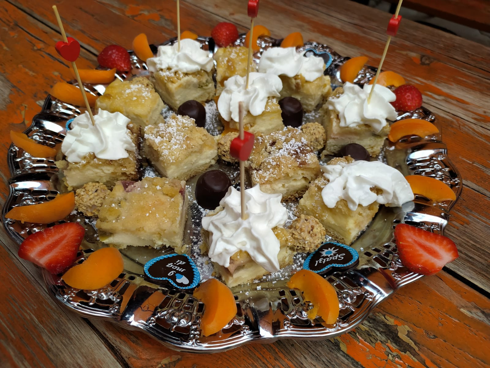 Ein Tablett mit Obstkuchenstücken, darauf Sahne, Schokoherzen, Erdbeeren und Aprikosen.