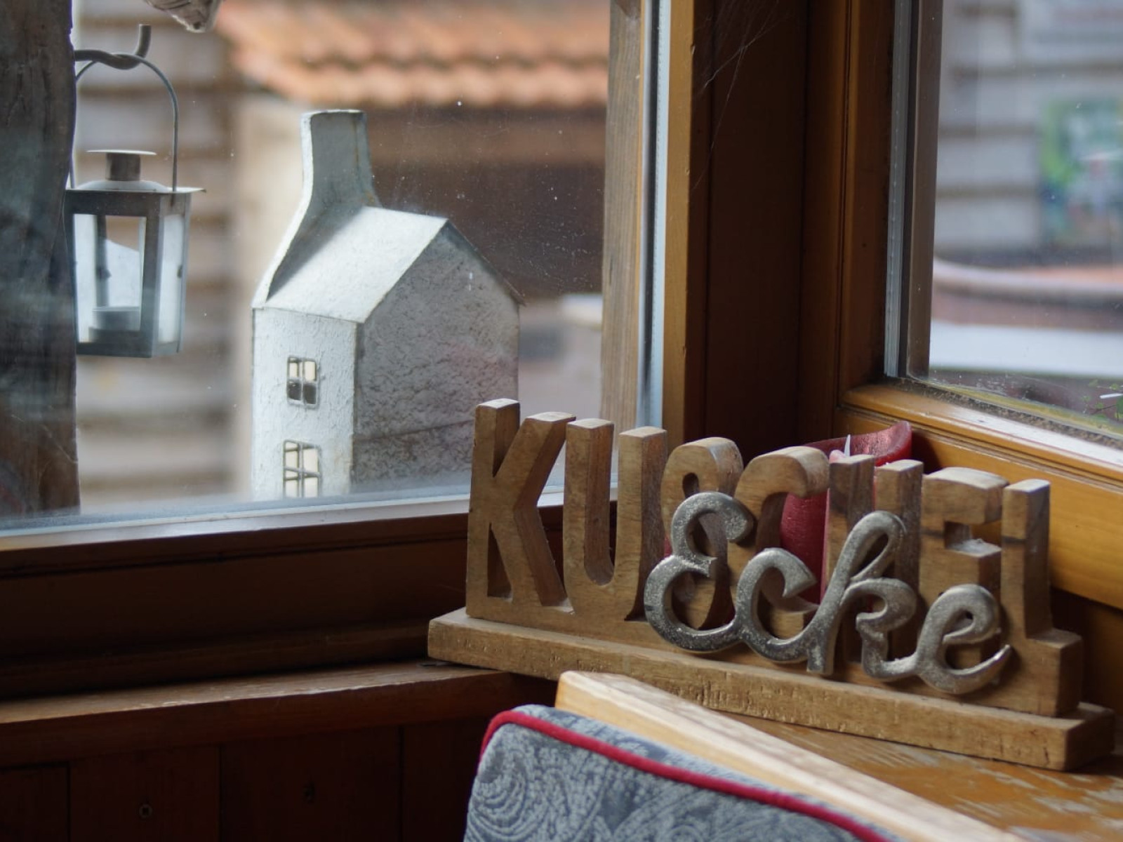 Holzschild 'Kuschelecke' auf der Fensterbank neben einer Laterne und einem kleinen Hausmodell.