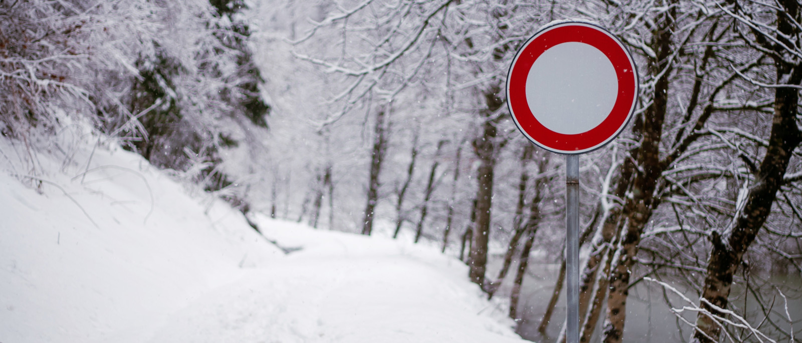 Schneebedeckter Weg mit rotem Verkehrsverbotsschild und Bäumen im Hintergrund.